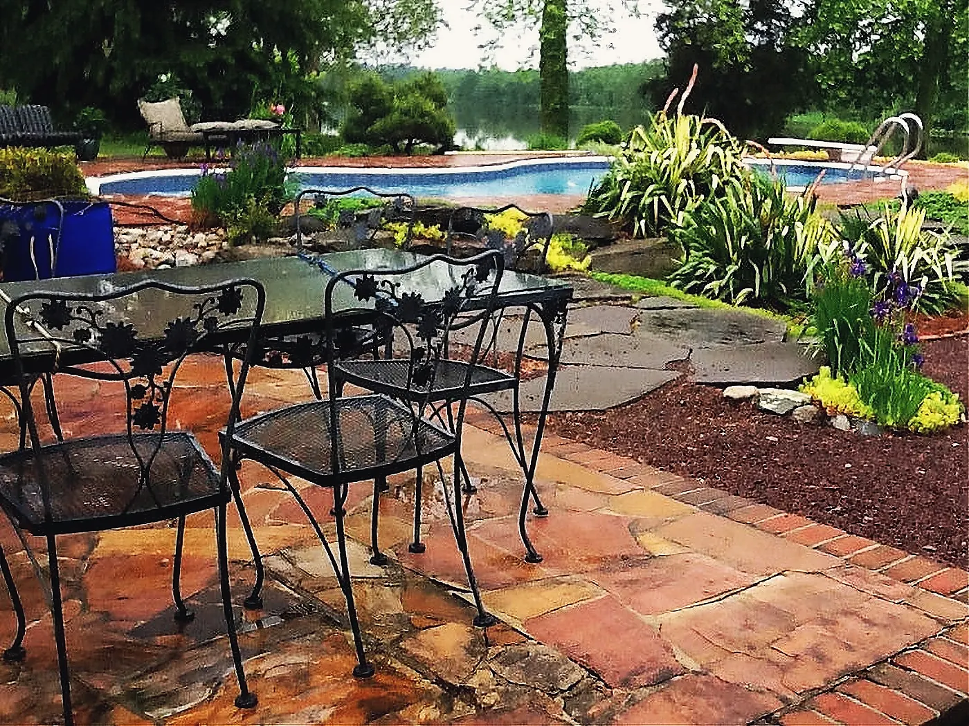 Flagstone and brick paving beside a pool, with iron chairs set out