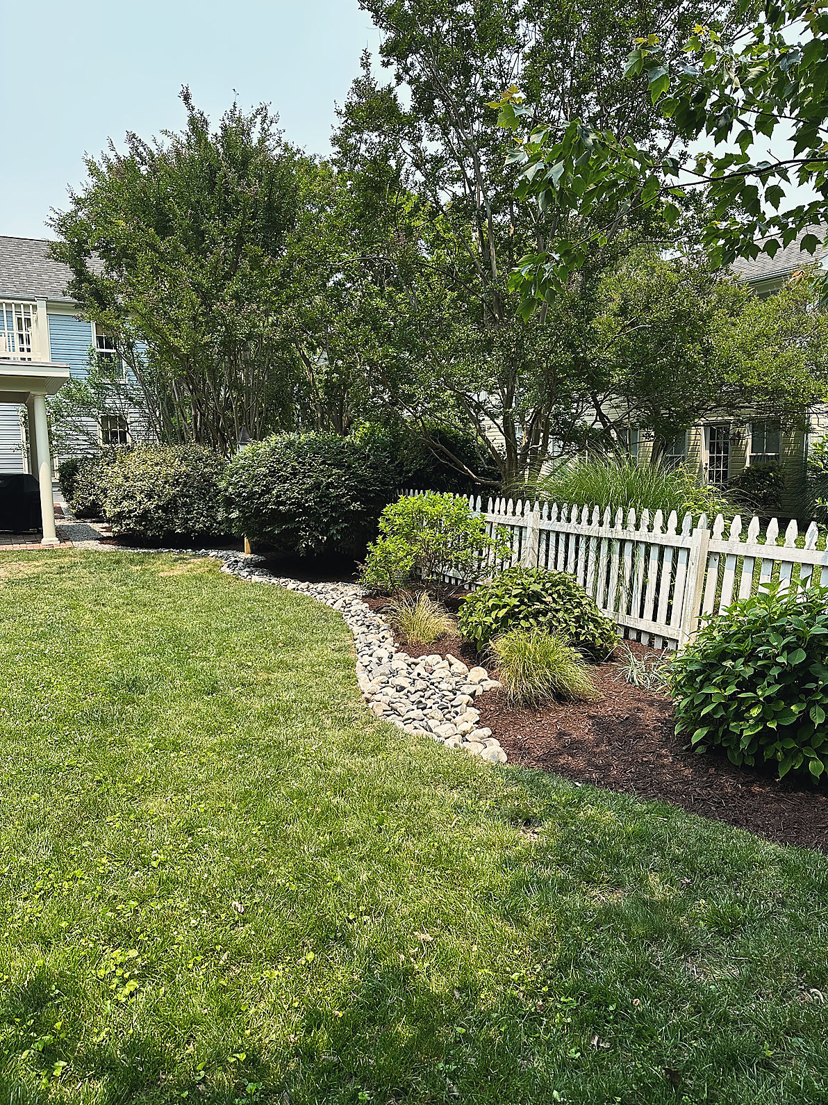 A curved bed line edged in river stone along a picket fence